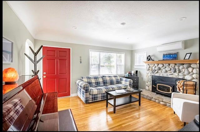 living room featuring a fireplace, wood-type flooring, a wall unit AC, and a textured ceiling