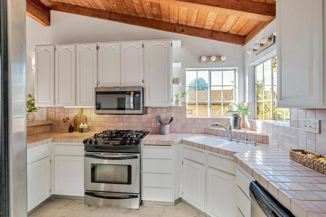 kitchen featuring sink, appliances with stainless steel finishes, white cabinetry, vaulted ceiling with beams, and tile countertops