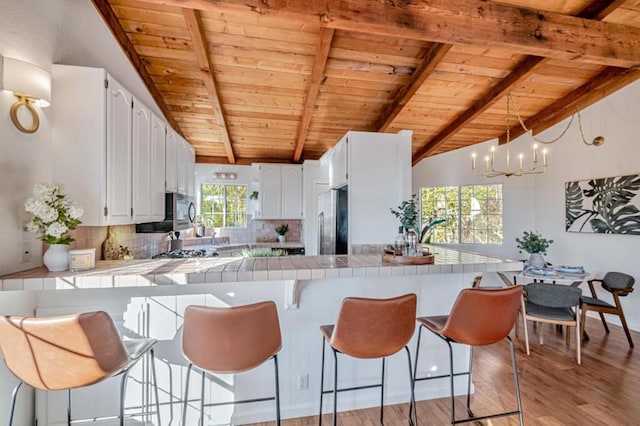 kitchen with vaulted ceiling with beams, white cabinetry, kitchen peninsula, stainless steel appliances, and decorative backsplash