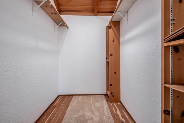 walk in closet with beamed ceiling and wood-type flooring