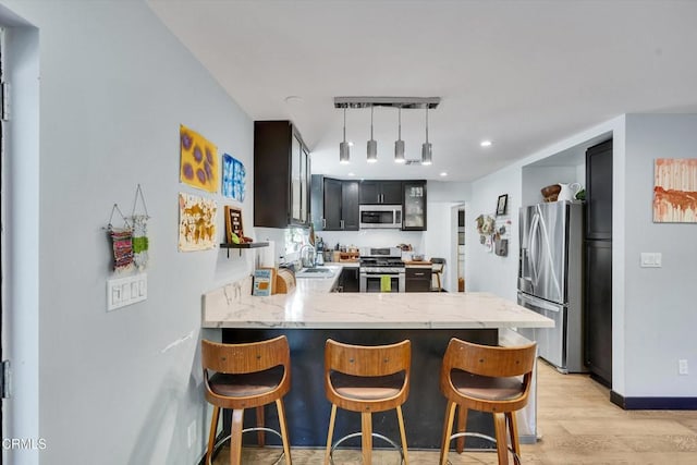 kitchen featuring stainless steel appliances, kitchen peninsula, a breakfast bar area, and light hardwood / wood-style flooring