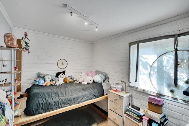 bedroom with rail lighting, brick wall, and ornamental molding