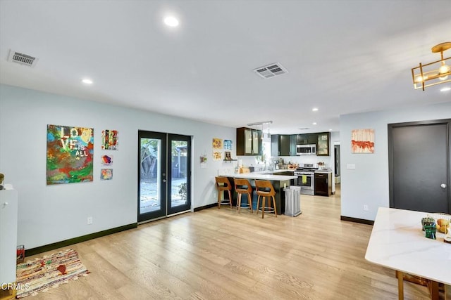 kitchen with french doors, a breakfast bar, light hardwood / wood-style flooring, kitchen peninsula, and stainless steel appliances