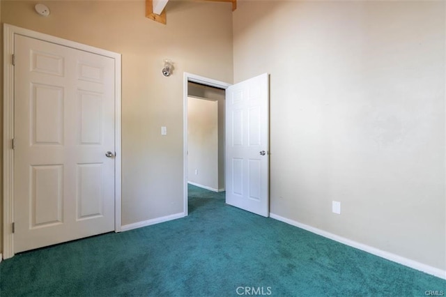 unfurnished bedroom featuring beamed ceiling, dark carpet, and a closet