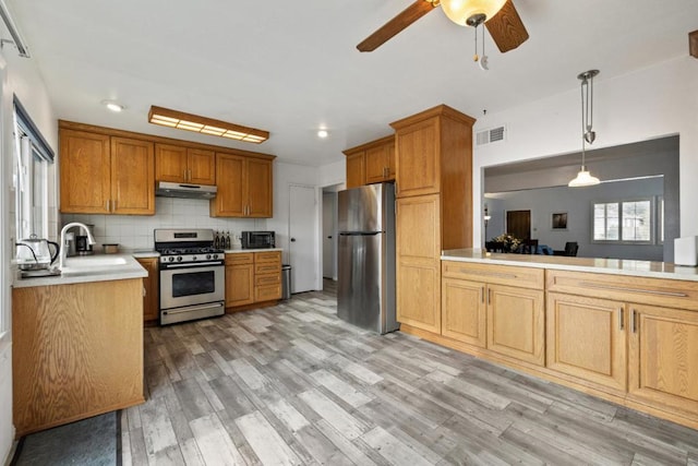 kitchen with pendant lighting, sink, light hardwood / wood-style flooring, appliances with stainless steel finishes, and backsplash