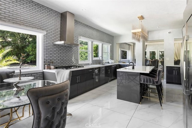 kitchen with sink, a breakfast bar area, stainless steel appliances, an island with sink, and wall chimney exhaust hood