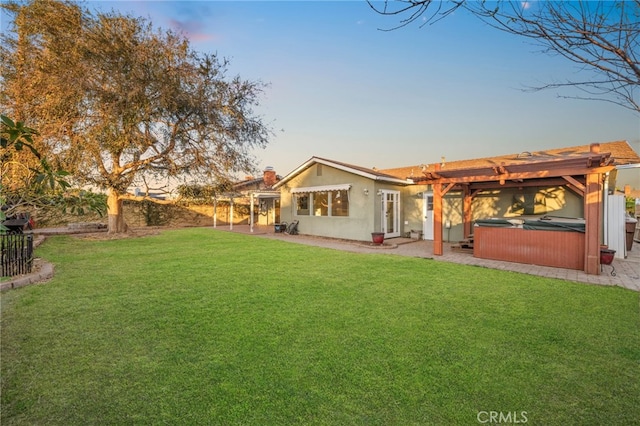 back house at dusk with a hot tub, a patio, and a lawn