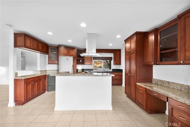 kitchen featuring light stone counters, island range hood, built in desk, light tile patterned floors, and a kitchen island