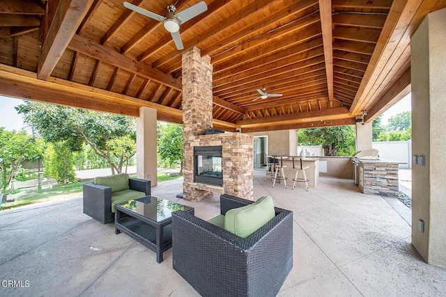 view of patio featuring area for grilling, ceiling fan, an outdoor bar, and an outdoor stone fireplace