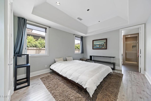 bedroom featuring ensuite bathroom, a tray ceiling, and light wood-type flooring