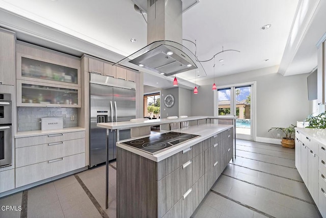 kitchen with appliances with stainless steel finishes, island range hood, a wealth of natural light, a kitchen island, and decorative backsplash