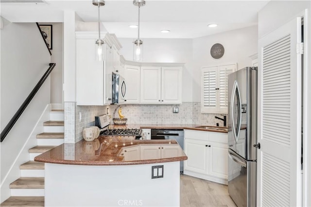 kitchen with pendant lighting, sink, white cabinets, kitchen peninsula, and stainless steel appliances