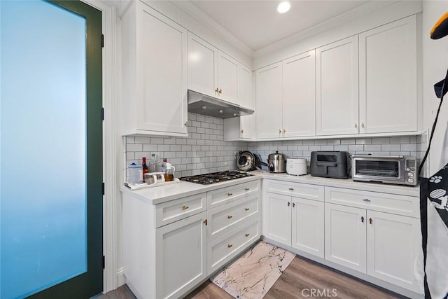 kitchen featuring white cabinetry, tasteful backsplash, ornamental molding, stainless steel gas cooktop, and light wood-type flooring