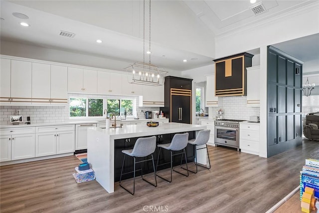 kitchen with white cabinetry, high end appliances, wood-type flooring, a kitchen island, and decorative backsplash