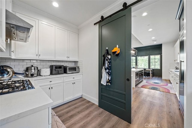 kitchen featuring tasteful backsplash, extractor fan, a barn door, and white cabinets