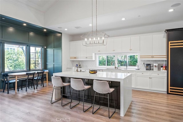 kitchen with white cabinetry, a kitchen island with sink, sink, and decorative light fixtures