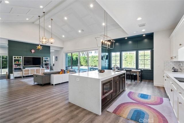 kitchen with white cabinetry, backsplash, a kitchen island with sink, hanging light fixtures, and plenty of natural light