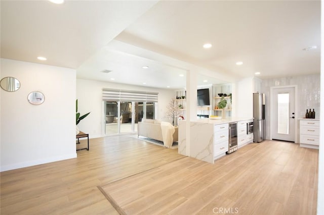 kitchen with white cabinetry, stainless steel fridge, beverage cooler, light stone counters, and light wood-type flooring