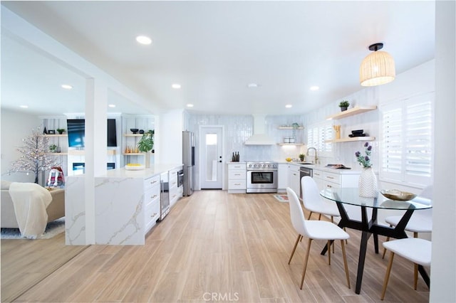 kitchen featuring premium range hood, sink, white cabinetry, light stone counters, and appliances with stainless steel finishes