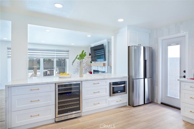 kitchen with stainless steel appliances, beverage cooler, light wood-type flooring, and white cabinets