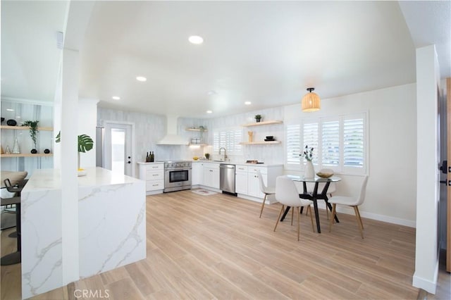 kitchen with premium range hood, sink, light stone counters, stainless steel appliances, and white cabinets