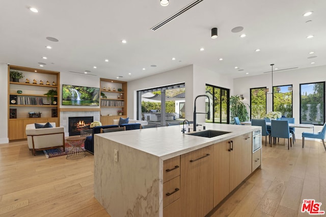 kitchen with sink, light hardwood / wood-style floors, a center island with sink, a tiled fireplace, and decorative light fixtures