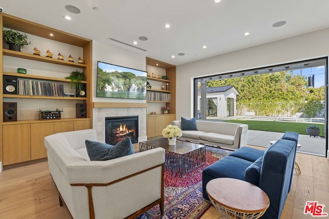 living room with built in features, light hardwood / wood-style flooring, and a tile fireplace