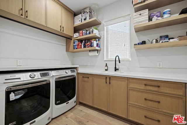 clothes washing area featuring sink, light hardwood / wood-style floors, cabinets, and washing machine and clothes dryer