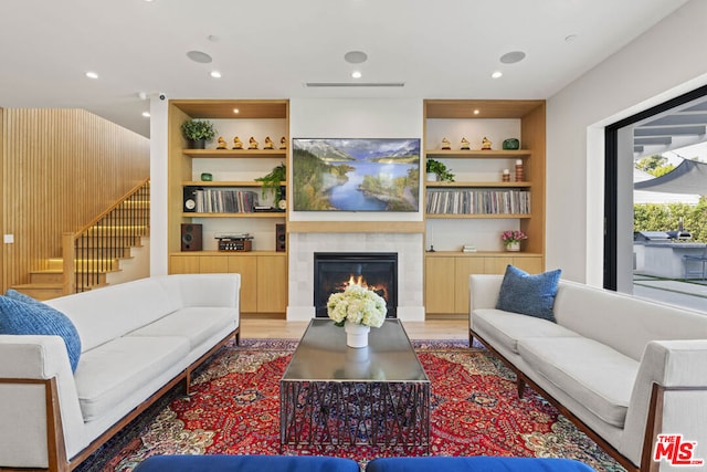 living room with built in features, a tile fireplace, and light wood-type flooring