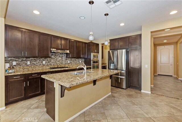 kitchen featuring appliances with stainless steel finishes, sink, a breakfast bar area, hanging light fixtures, and a center island with sink