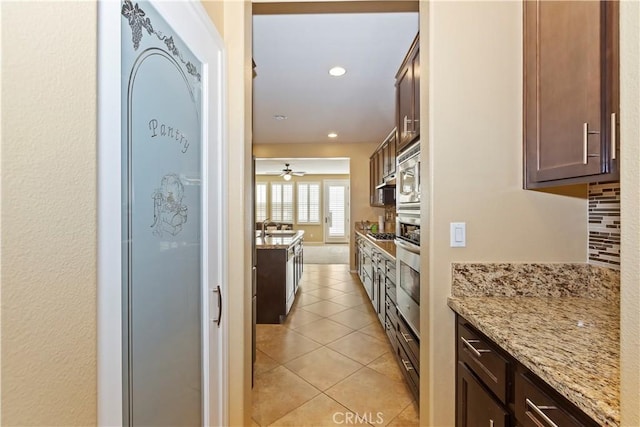 kitchen featuring sink, light stone counters, dark brown cabinets, light tile patterned floors, and decorative backsplash