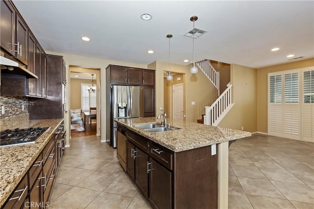 kitchen featuring decorative light fixtures, sink, a kitchen island with sink, stainless steel appliances, and light stone countertops