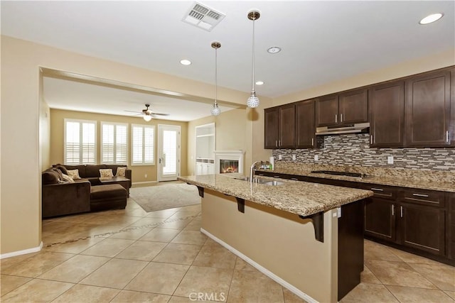 kitchen with a breakfast bar, light stone counters, hanging light fixtures, a kitchen island with sink, and black stovetop