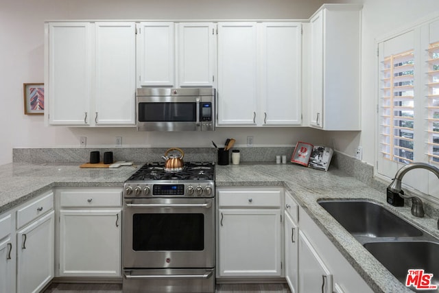 kitchen with white cabinetry, appliances with stainless steel finishes, light stone countertops, and sink