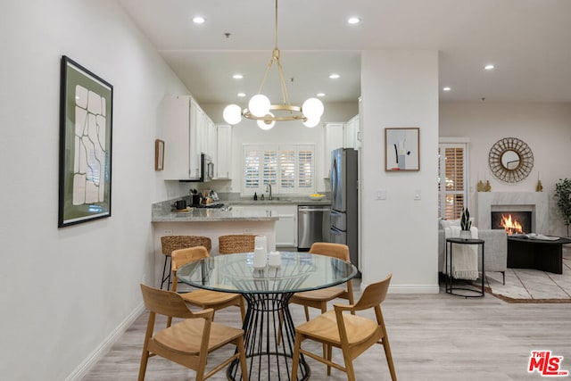 dining room featuring a fireplace, sink, light hardwood / wood-style flooring, and a notable chandelier