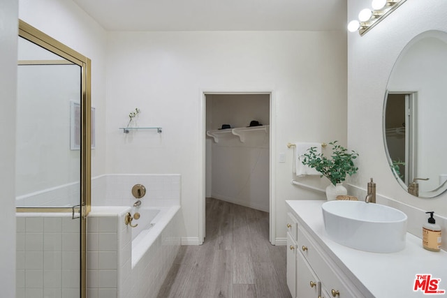 bathroom with a relaxing tiled tub, wood-type flooring, and vanity