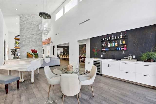 dining area featuring light hardwood / wood-style floors, wet bar, beverage cooler, and a high ceiling