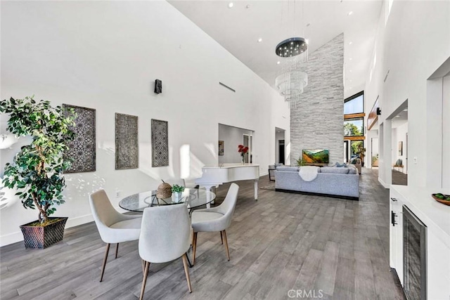 dining area featuring an inviting chandelier, a towering ceiling, wood-type flooring, and beverage cooler