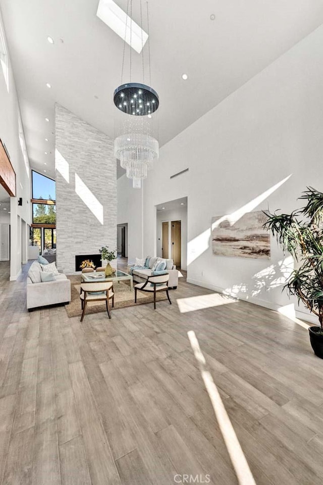 living room with a stone fireplace, a towering ceiling, a skylight, a notable chandelier, and light hardwood / wood-style floors