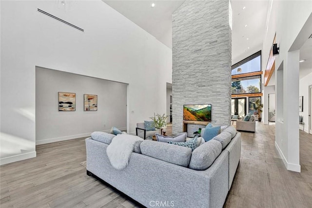 living room with a stone fireplace, light hardwood / wood-style flooring, and high vaulted ceiling