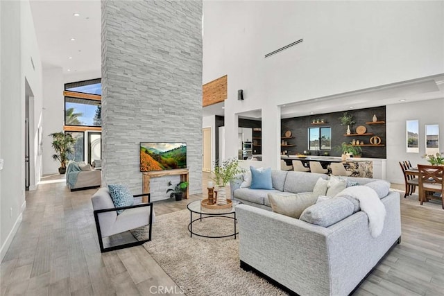 living room featuring a towering ceiling, a large fireplace, and light wood-type flooring