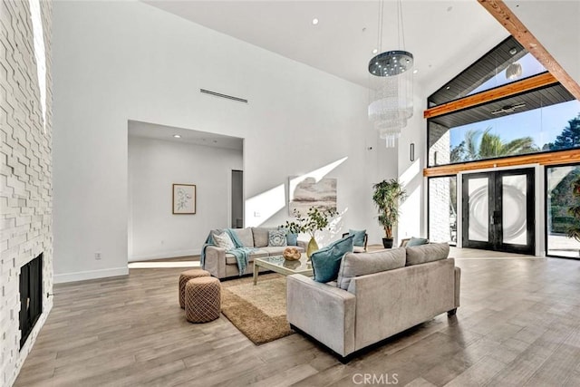 living room with hardwood / wood-style floors, a fireplace, high vaulted ceiling, a chandelier, and french doors