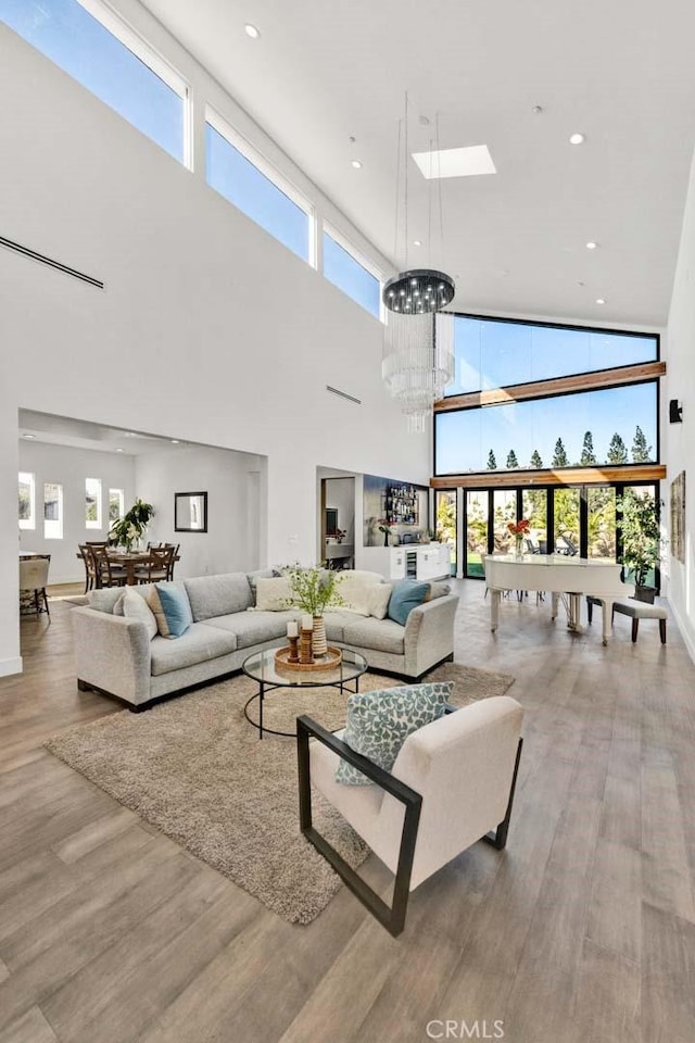 living room featuring a towering ceiling, a skylight, light hardwood / wood-style floors, and a chandelier