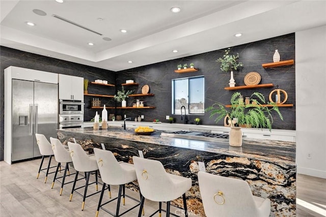 kitchen with stainless steel appliances, a raised ceiling, white cabinets, and a kitchen breakfast bar