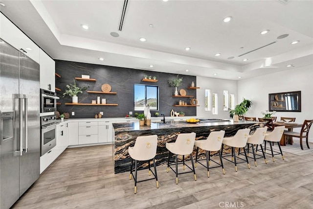 kitchen with white cabinetry, appliances with stainless steel finishes, a raised ceiling, and a breakfast bar area