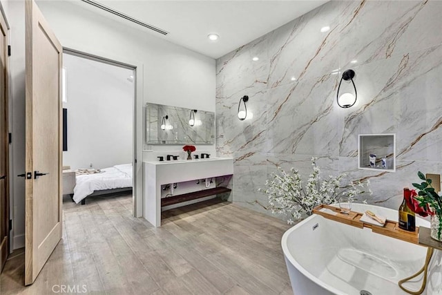 bathroom with hardwood / wood-style flooring, vanity, a bath, and tile walls