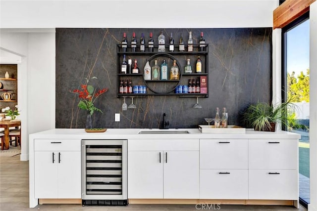 bar with white cabinetry, sink, wine cooler, and light wood-type flooring