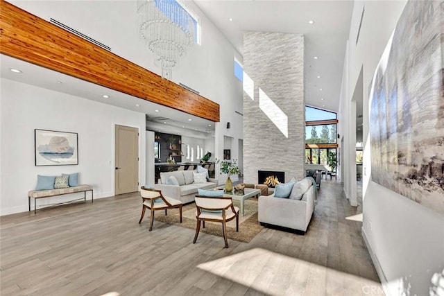 living room with a towering ceiling, a fireplace, a chandelier, and light wood-type flooring