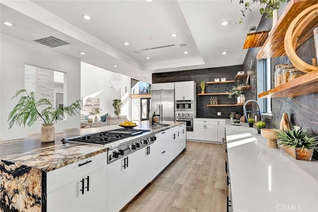 kitchen with appliances with stainless steel finishes, white cabinetry, sink, a raised ceiling, and light hardwood / wood-style flooring