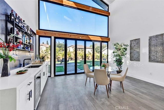 dining space featuring hardwood / wood-style floors, a towering ceiling, sink, and wine cooler